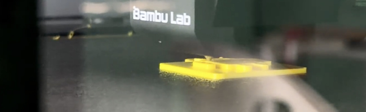 A Bambu Lab 3D printer part-way through printing a yellow component.